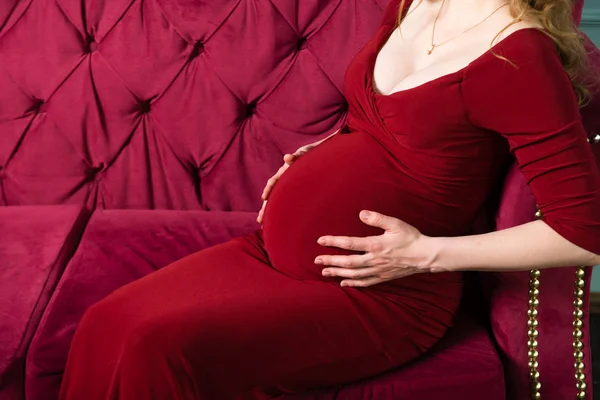 Belly of a pregnant woman with hugging hands in a red dress — Stock Photo, Image