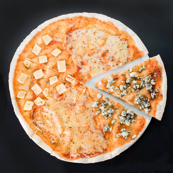 Sliced pizza with different kinds of cheese on a dark background