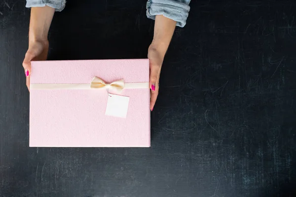 Manos femeninas sosteniendo una caja en forma cuadrada con un regalo en — Foto de Stock