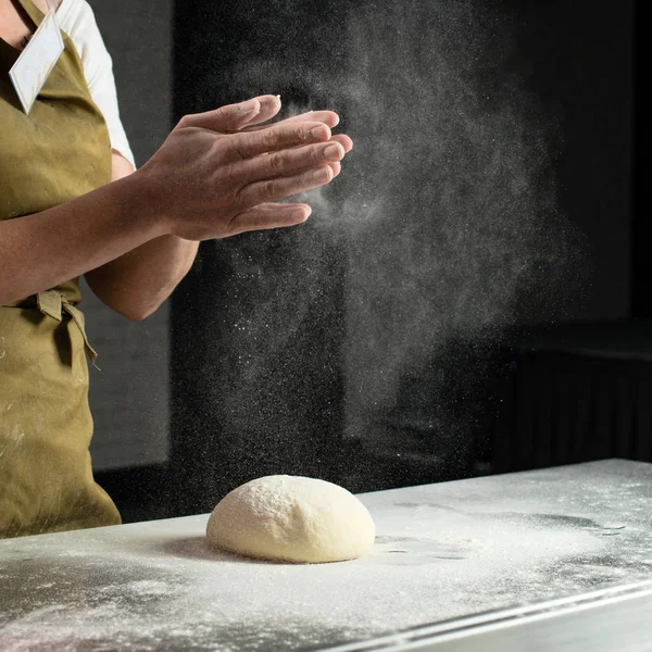 woman baker sprinkled flour on roll dough on a wooden board. Pro