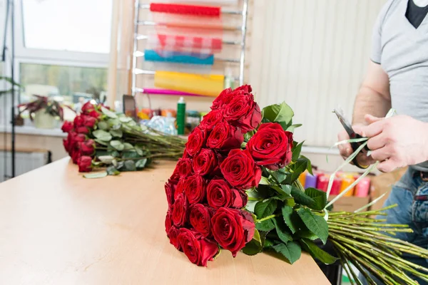 Florista no trabalho fazendo um buquê de rosas vermelhas. foco no bouq — Fotografia de Stock