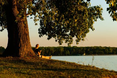 t arka planda büyük bir ağaç içinde oturan genç sarışın kadın