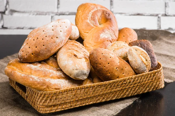 Différents types de pain frais dans un panier sur une table, brique backg — Photo