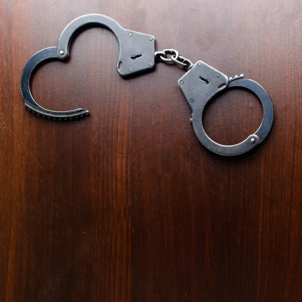 Steel police handcuffs lying on the wooden table, top view, copy — Stock Photo, Image