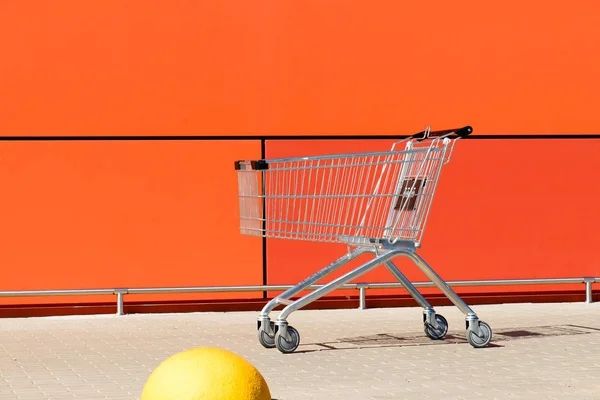 Carrello della spesa vuoto in metallo vicino alla parete arancione della spesa c — Foto Stock