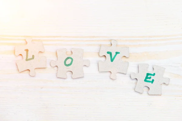 Word Love made of four pieces of jigsaw puzzle on light wooden t