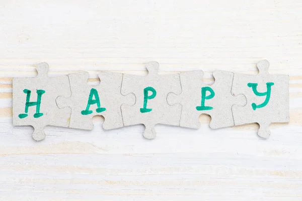 Слово Щасливий з чотирьох шматочків головоломки на світлому дерев'яному — стокове фото