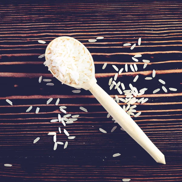 Raw and uncooked white rice in wooden spoon on wood background. — Stock Photo, Image