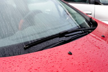 Cam silecekleri ışınları içinde yağmur sonra damla ile kırmızı bir araba 