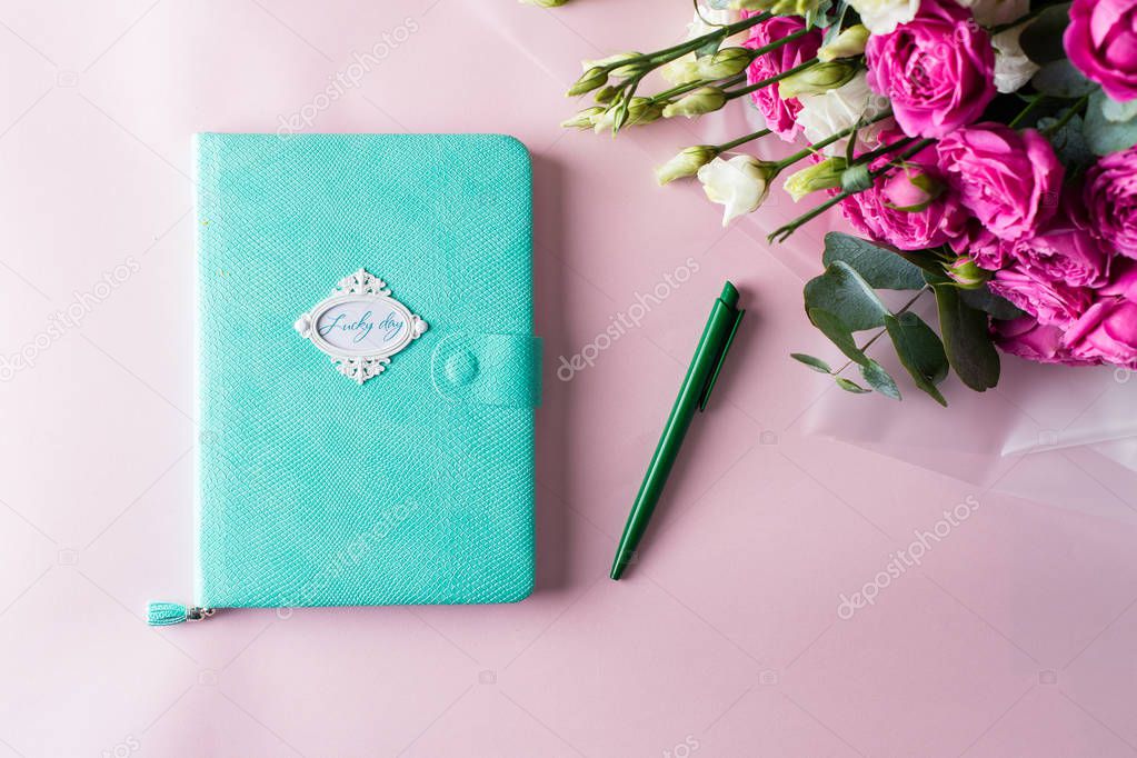 Woman diary, pen and beautiful flowers on pink table, top view, 