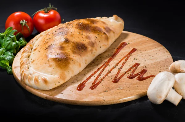 Lezzetli Pizza calzone fesleğen ile dar ahşap tahta üzerinde yapraklar