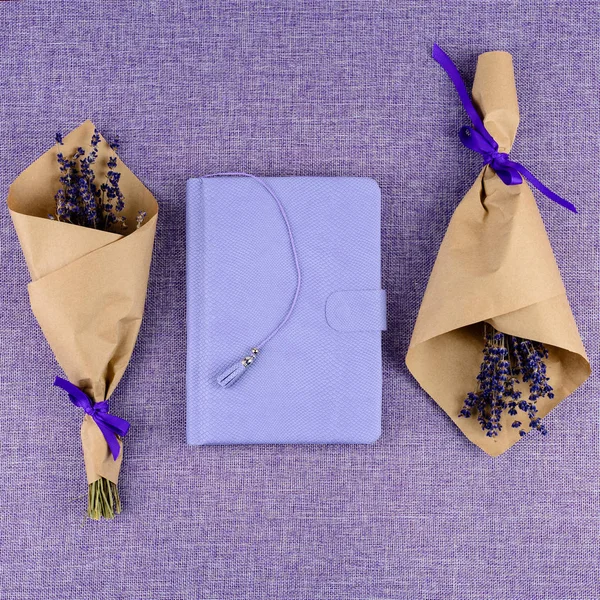 Purple closed notebook and bouquets of flowers on purple backgro