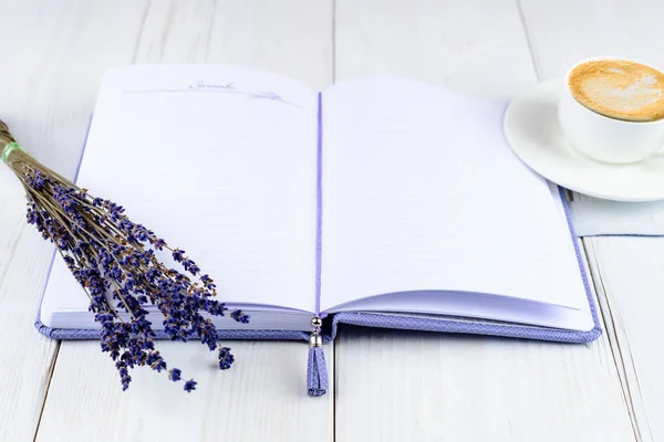 Notebook roxo, xícara de café e flores em backg de madeira leve — Fotografia de Stock