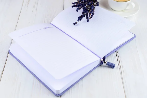 Purple notebook, cup of coffee and flowers on light wooden backg — Stock Photo, Image