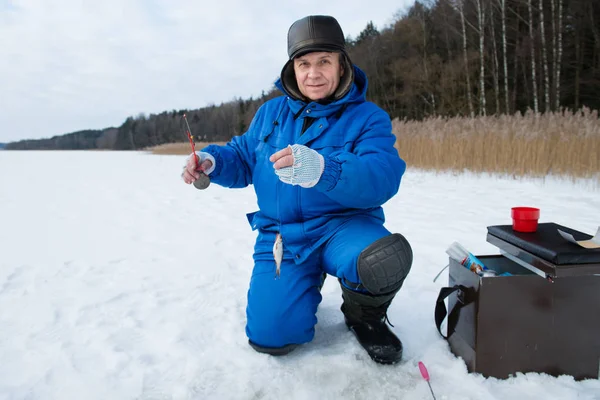 Homem sorrindo positivo pesca em um lago no dia de inverno frio — Fotografia de Stock