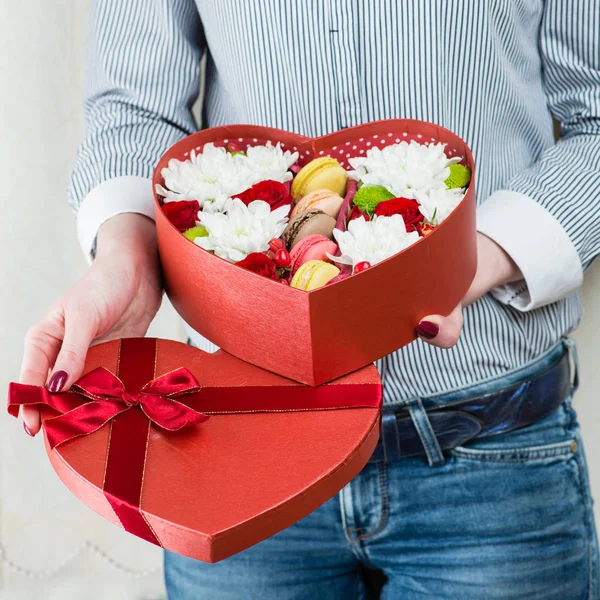 Caja-corazón roja con flores y macarrones en manos femeninas close-u — Foto de Stock