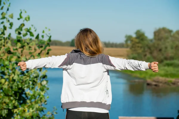 Young woman raising hands up against nature background