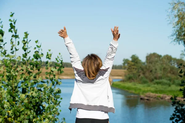 Young woman raising hands up against nature background