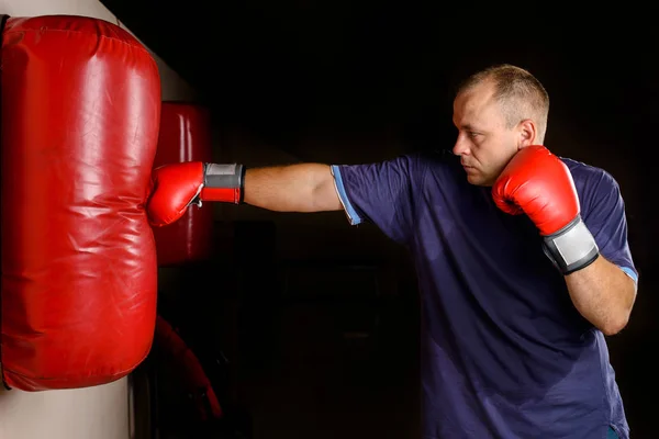 novice male boxer training with punching bag on dark background. Male boxer as exercise for the big fight.