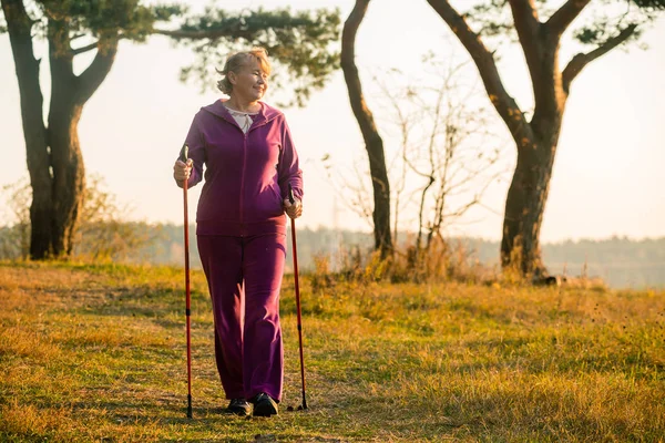 Sport in Finland - Nordic walking. Senior Woman hiking in forest or park. Active and healthy lifestyle.