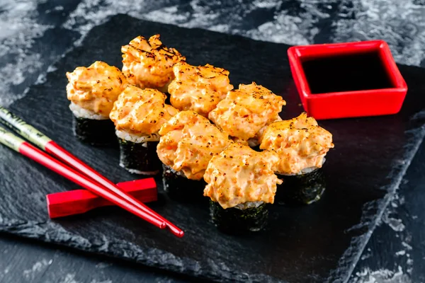 baked sushi roll on black stone served with chopsticks and soy