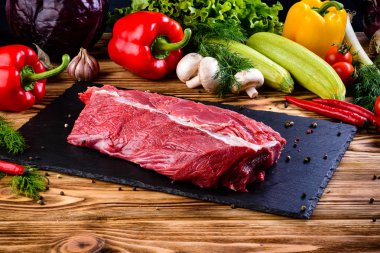 Natürmort taze çiğ sığır eti biftek malzemelerle karanlık masada yemek pişirmek için bir kesme tahtası üzerinde. kopya alanı. Ham sığır eti kalın kaburga, bonfile ve kürek kemiği