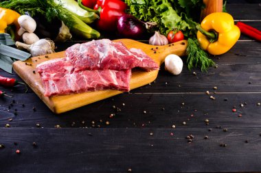 Çiğ domuz eti. Metniniz için koyu arka plan ve kopya alanı üzerinde ahşap kesme tahtası üzerinde taze biftek bonfile. Sebze ve baharatlar ile ham kaburga eti