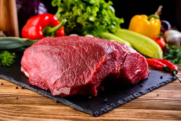 Still life fresh raw beef meat steak on a cutting board with ingredients for cooking on dark table. Raw beef thick rib, tenderloin and shoulder blade