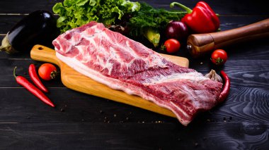 Çiğ domuz eti. Metniniz için koyu arka plan ve kopya alanı üzerinde ahşap kesme tahtası üzerinde taze biftek bonfile. Sebze ve baharatlar ile ham kaburga