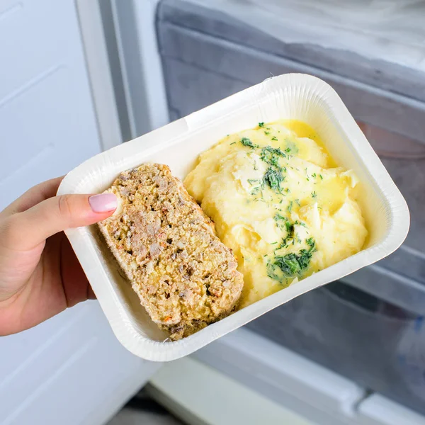 frozen food from the freezer in the female hand, Woman placing container with frozen ready meals in refrigerator, Poultry meat bread and mashed potatoes