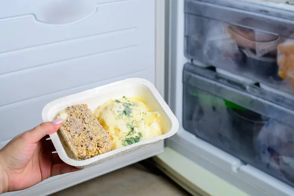 frozen food from the freezer in the female hand, Woman placing container with frozen ready meals in refrigerator