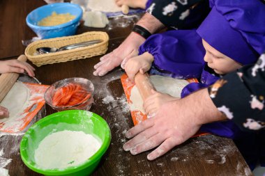 Yetişkin el pizza yapmak için bir çocuk öğretiyor, oğlu mutfak masasında ekmek rulo. A Family ev yapımı pizza pişirimiyapıyor..