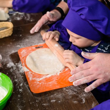 Yetişkin el pizza yapmak için bir çocuk öğretiyor, oğlu mutfak masasında ekmek rulo. A Family ev yapımı pizza pişirimiyapıyor..