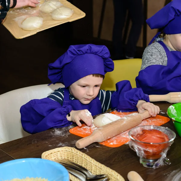 Cute little boy with chef hat standing at table kneading bread dough — Stock Photo, Image