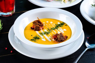 Kabak ve havuç kremalı çorba ve siyah ahşap zemin üzerine beyaz kase baharat görünümü top