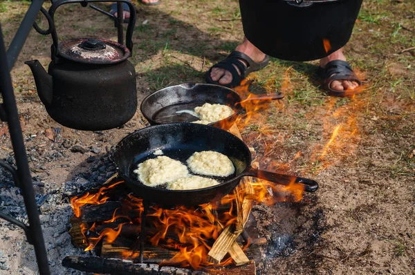 Kochen auf einem Feuer im Wald. auf dem Gitter befinden sich Topf und Pfanne. in einer Pfanne gebratene Pfannkuchen — Stockfoto