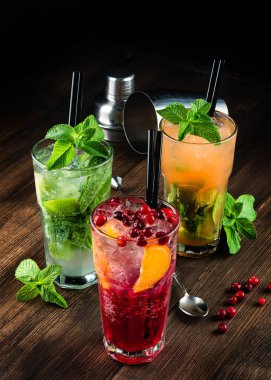 Üç alkollü mojito ve kızılcık kokteyli veya ahşap bir arka planda yaban mersini kokteyli, buzlu mojito kokteyli ve nane şekeri. Kızılcıkla süslenmiş kokteyl.