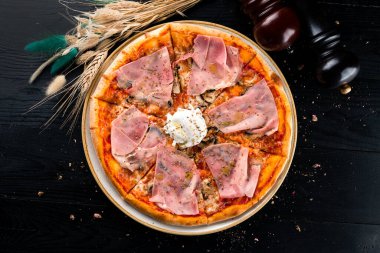 Jambonlu ve haşlanmış yumurtalı İtalyan pizzası, pastırmalı Capricciosa pizzası, siyah arka planda jambon, düz uzanmış.