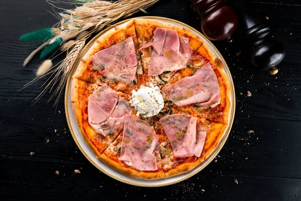 Jambonlu ve haşlanmış yumurtalı İtalyan pizzası, pastırmalı Capricciosa pizzası, siyah arka planda jambon, düz uzanmış.