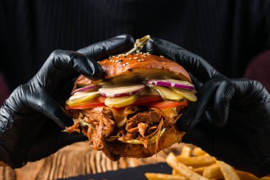 Siyah eldivenli kadın eller taze lezzetli bir burger tutuyor. Salata ve patates kızartmalı burger, fast food yiyen bir kız..