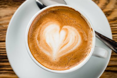 Tahta arka planda beyaz bir fincanda kalp desenli bir fincan kahve, aşk desenli bir kahve.