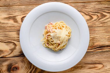 Makarna dolu beyaz bir kâse yakın çekim. Tabakta İtalyan makarnası, ahşap masa üstü manzaralı, düz uzanmış.