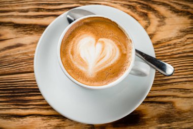 Tahta arka planda beyaz bir fincanda kalp desenli bir fincan kahve, aşk desenli bir kahve.