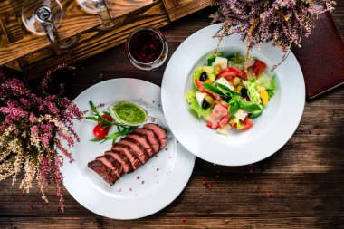 Ahşap masada sebze salatalı barbekü bifteği, iki çeşit öğle yemeği eteği bifteği ve sebze salatası üst görünümü, düz uzanmış.