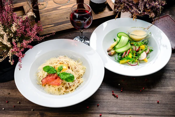 Lezzetli yemek. İtalyan makarnası. Sağlıklı yiyecekler. Kapatın. Pastırmalı, peynirli, turplu ve otlu taze salatalı iki tabak makarna.