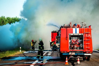 İtfaiyeci kazadan sonra yanan bir arabayı söndürür. İtfaiyeci su ve yangın söndürücü kullanır. İtfaiyeci yangın söndürücü kullanır.