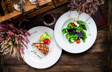 Masada iki tabak biftek ve salata, restoranda öğle yemeği, ızgara ton balığı manzarası, düz uzanma.
