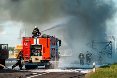 İtfaiyeci kazadan sonra yanan bir arabayı söndürür. İtfaiyeci su ve yangın söndürücü kullanır. İtfaiyeci yangın söndürücü kullanır.