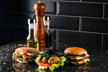 Koyu arkaplanda farklı ekmekleri olan üç hamburger fotokopi alanı için siyah arka planda farklı yeni hamburgerler.