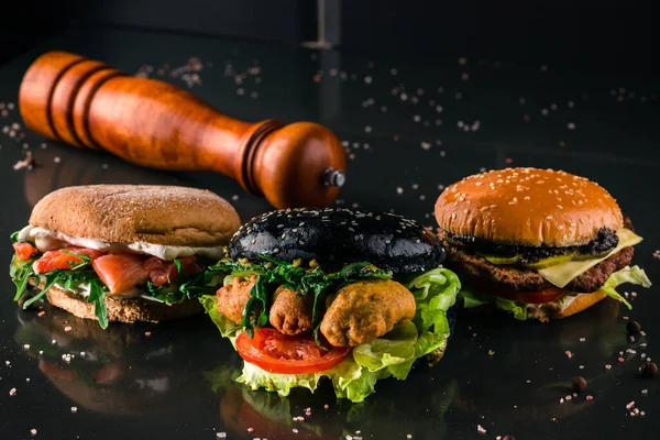 Three burgers with different bread buns on dark background, different new burgers against black background for copy space